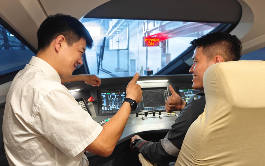 8月25日，在印度尼西亞萬隆的雅萬高鐵德卡魯爾動車所內(nèi)，中國師傅穆振（左）在向印尼火車司機塞蒂亞萬講解動車組出庫前的上電作業(yè)。