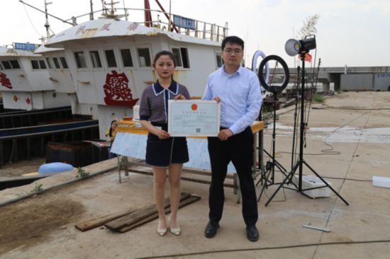 海鮮電商張夢琴與幫辦員手持食品經營許可證合影。贛榆區(qū)委宣傳部供圖